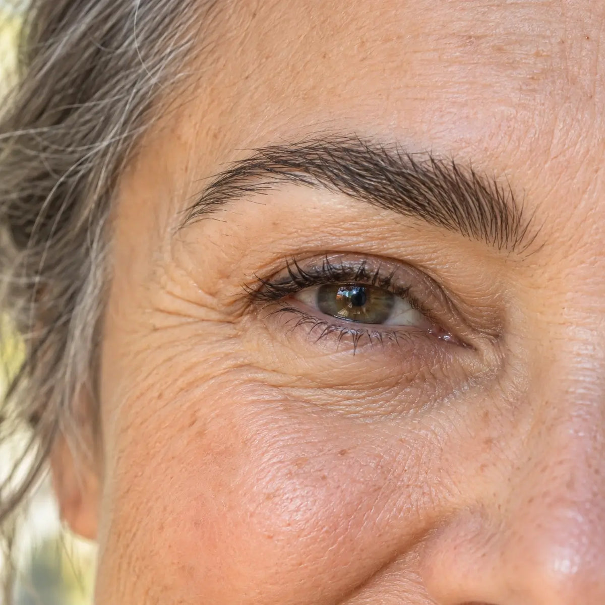 Illustrative close-up of a smiling mature woman with a natural full brow; an appearance goal, not a product result